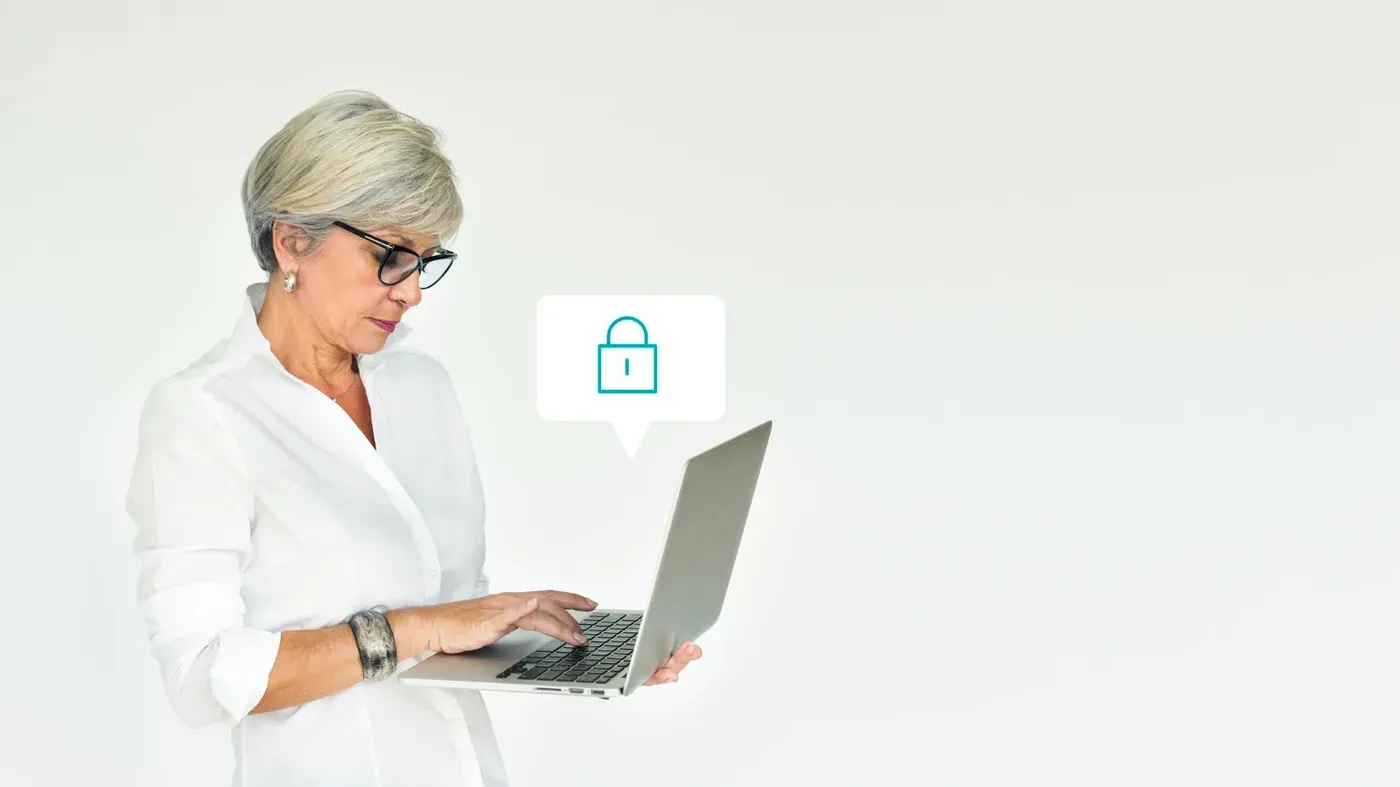 A senior professional woman with short grey hair and glasses standing while using a laptop, accompanied by a digital padlock icon representing security.